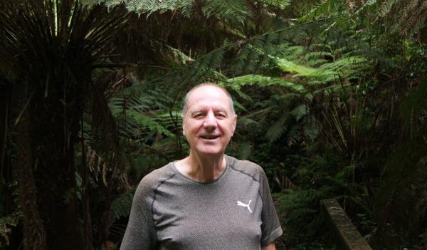 Volunteer member of the Friends of Mount Worth State Park Tony Castle stands on a bridge surrounded by lush tree ferns.